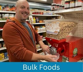 Smiling man using grinder to make almond butter in co-op's bulk area.